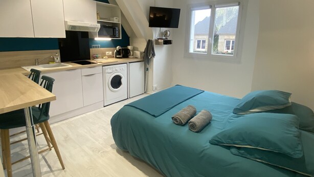 Una habitación compacta con cama, kitchenette pequeño, lavadora y televisión.