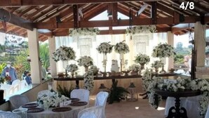 An outdoor covered dining area with tables set for a wedding reception, adorned with white floral arrangements and candle holders.