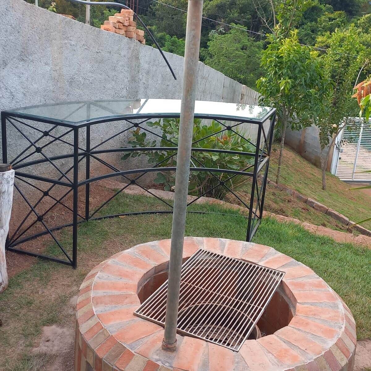 Un horno de ladrillo al aire libre con una parrilla metálica, una mesa de vidrio y una estructura de armazón metálico.