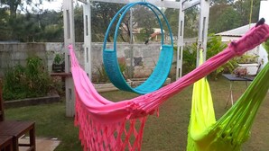 A hammock in a backyard with a white pergola, a wooden bench, and a table with a plant.