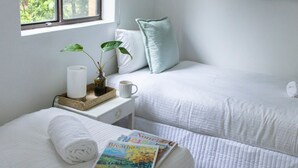 A bedroom with two beds, a bedside table with a plant, a candle, and a magazine. - Gidgets on Gretel - pet-friendly coastal cottage near Shoal Bay (Nelson Bay)