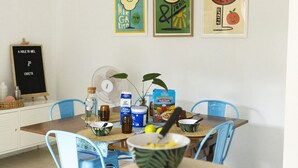 A dining area with a table set for two, featuring a fan, a bottle, a bowl, and a box of cereal. - Gidgets on Gretel - pet-friendly coastal cottage near Shoal Bay (Nelson Bay)