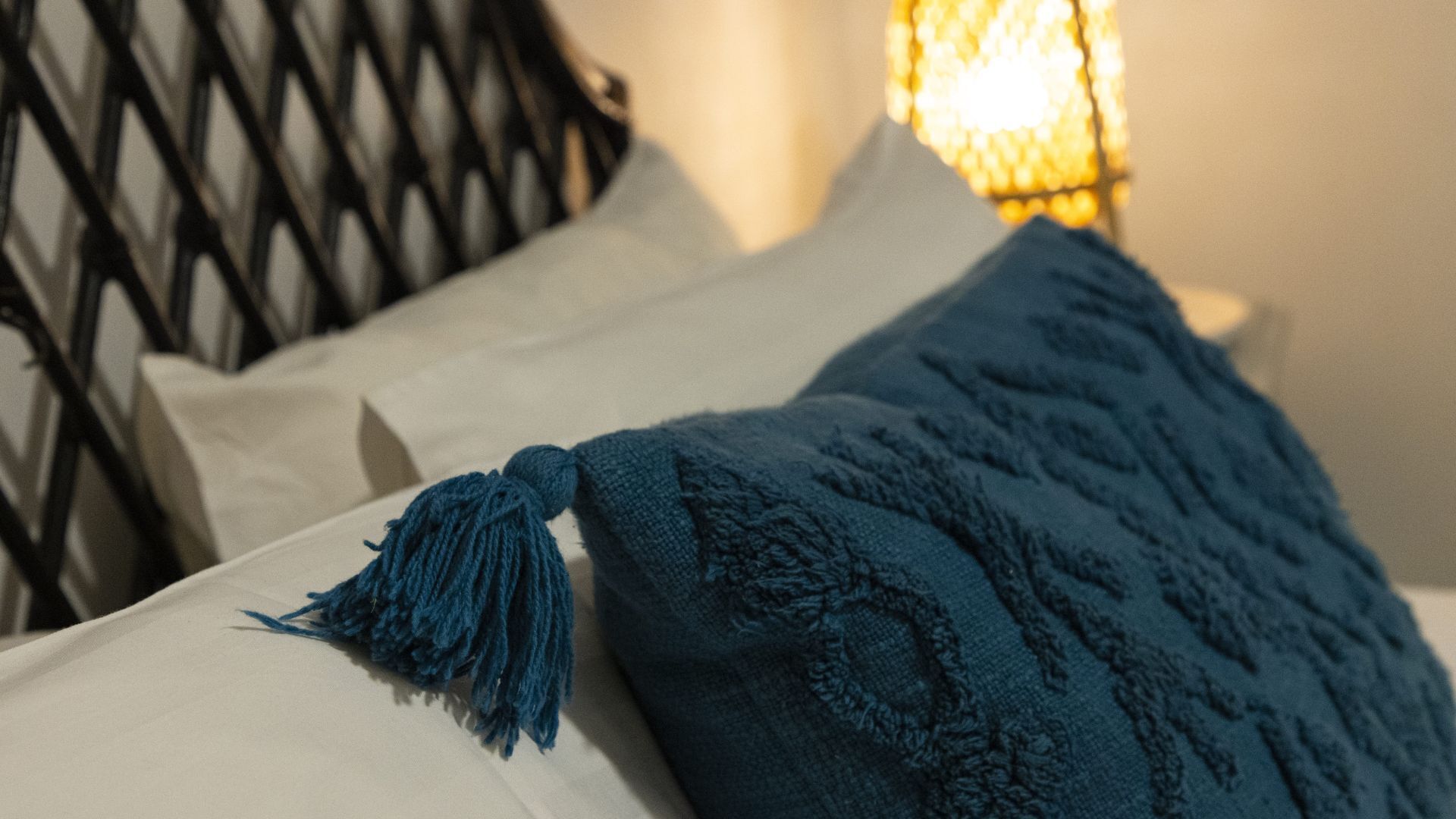 A bed with white pillows and a blue blanket with a tassel.