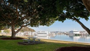 A marina with boats docked, a grassy area with benches, and trees providing shade. - Gidgets on Gretel - pet-friendly coastal cottage near Shoal Bay (Nelson Bay)