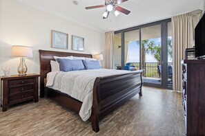 A bedroom with a bed, nightstands, a ceiling fan, and a view of the outdoors.