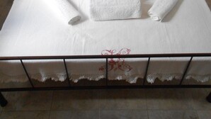 Uma cama bem arrumada com lençóis brancos, almofadas decorativas e uma mesa de cabeceira com abajur.