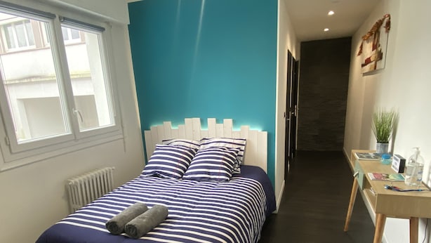 Ein Schlafzimmer mit einem Bett, einem Nachttisch mit Pflanze und einem Fenster.