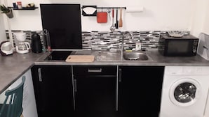 Eine kleine Küche mit Waschmaschine, Mikrowelle, Kaffeemaschine und Schneidebrett.