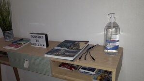Ein Schreibtisch mit einem Schild, das 'DONEMAT EN BREIZH' zeigt, einem Buch, einem Stift, einer Handdesinfektionsmittel-Flasche und einer Topfpflanze.