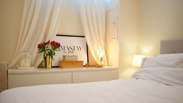 A neatly arranged bedroom with a bed, a bedside table with a vase of flowers, a lamp, and a framed sign. - Cozy 1 Bedroom Home Near the City Centre (Edinburgh)