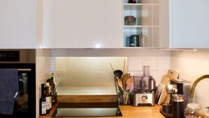 A modern kitchen with white cabinets, a built-in oven, a sink, and various kitchen appliances. - Cozy 1 Bedroom Home Near the City Centre (Edinburgh)