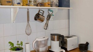 A kitchen with a wooden countertop, a coffee maker, a toaster, a kettle, a plant, and jars of spices on shelves. - Cozy 1 Bedroom Home Near the City Centre (Edinburgh)