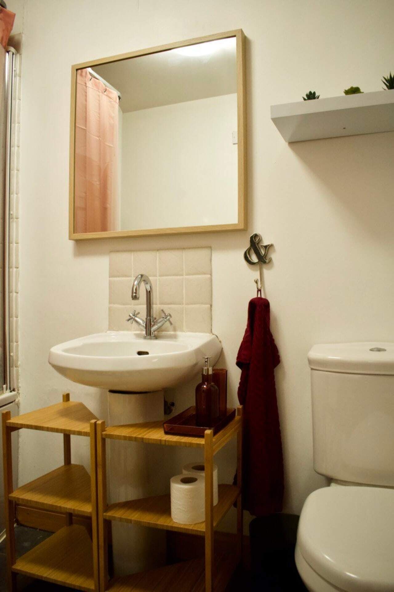 A bathroom with a white sink, a mirror, a toilet, and a wooden shelf with a red towel.