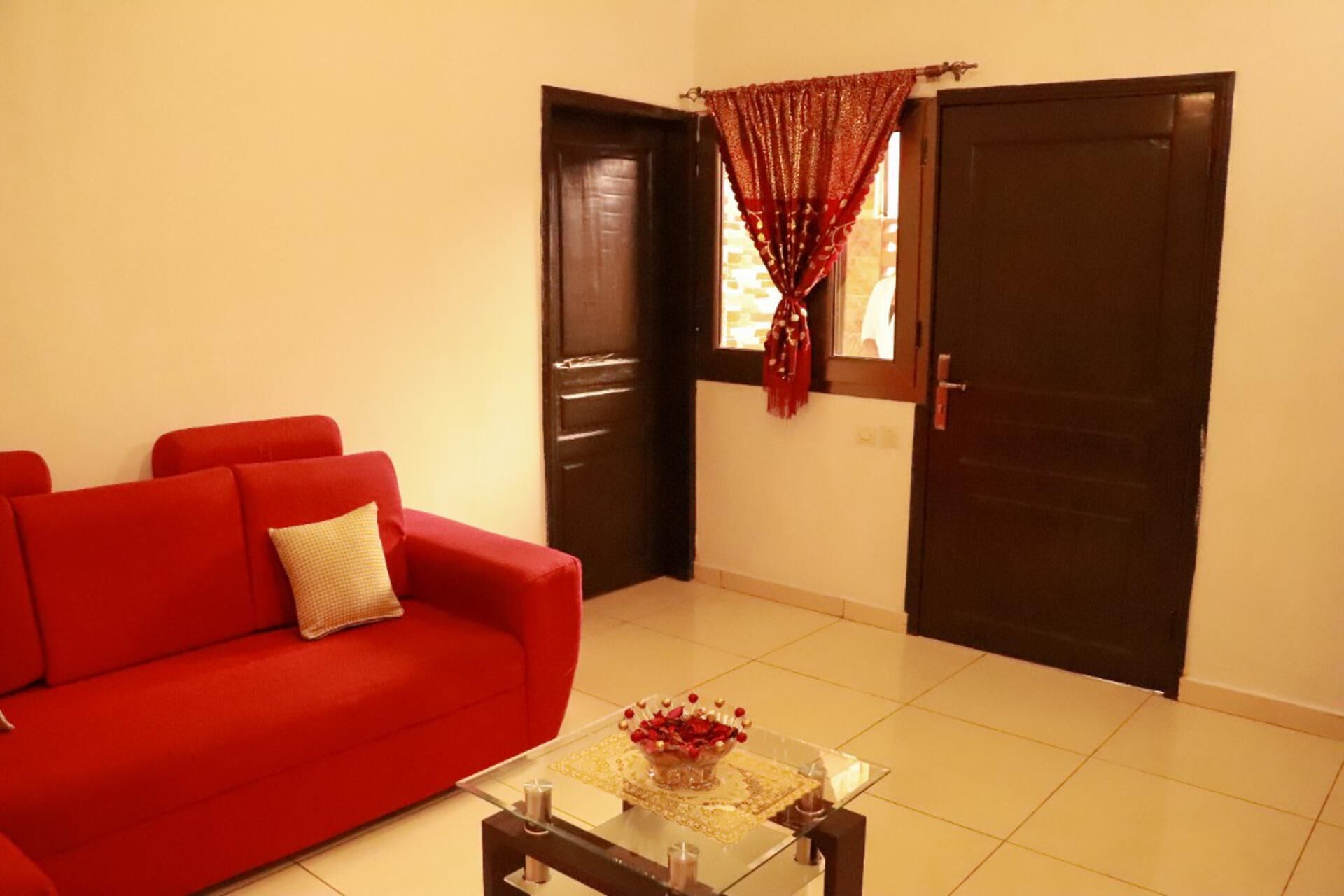 Un salón con un sofá rojo, una mesa de centro de vidrio con un cuenco decorativo y dos puertas de madera oscura.
