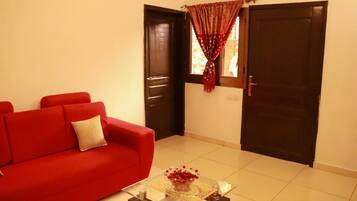 Un salón con un sofá rojo, una mesa de centro de vidrio con un cuenco decorativo y dos puertas de madera oscura.