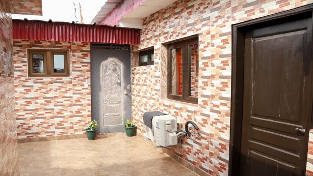 A courtyard with a brick wall, a door, and a window. There are two potted plants and a water heater. - Residence Appartements Luxueux - Angre - Abidjan (Abidjan)