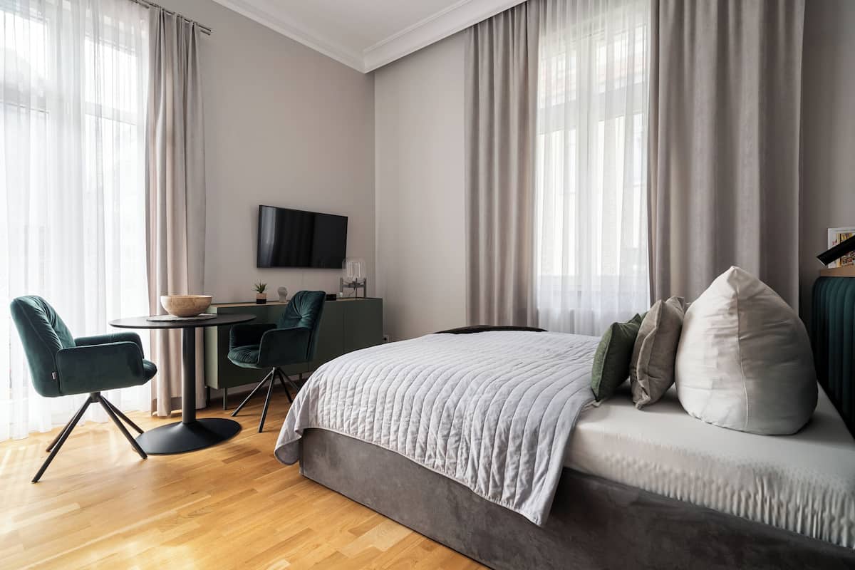 A modern hotel room with a large bed, a desk with a chair, a flat-screen TV, and a large window with curtains.