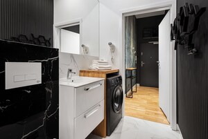 Un baño moderno con lavamanos de mármol negro, armarios blancos y lavadora integrada.