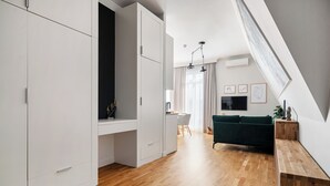Ein moderner Wohnraum mit weißen Schränken, Holzboden und einem grünen Sofa. Im Hintergrund ist ein Essbereich zu sehen.