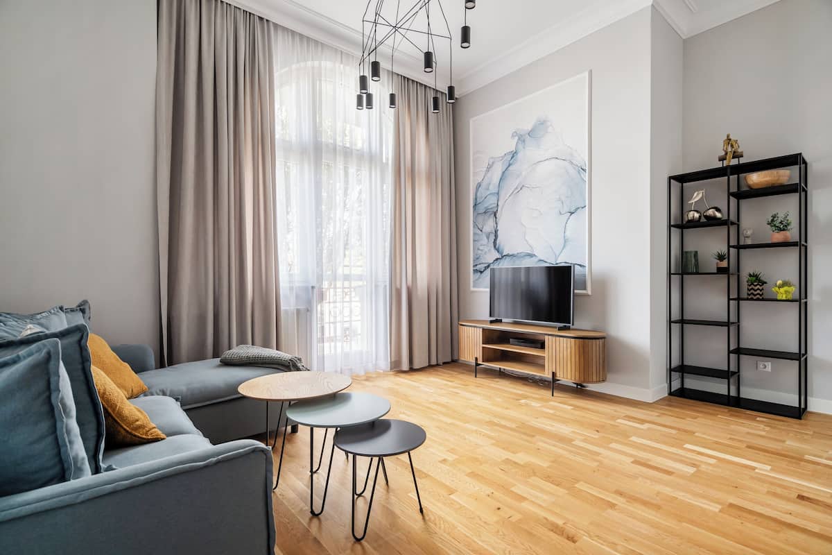 A modern living room with a grey sofa, two small round tables, a TV on a wooden stand, and a black shelving unit with decorative items.