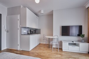 Una cocina moderna con armarios blancos, una mesa de comedor con sillas, un televisor en la pared y un mueble pequeño con una planta.