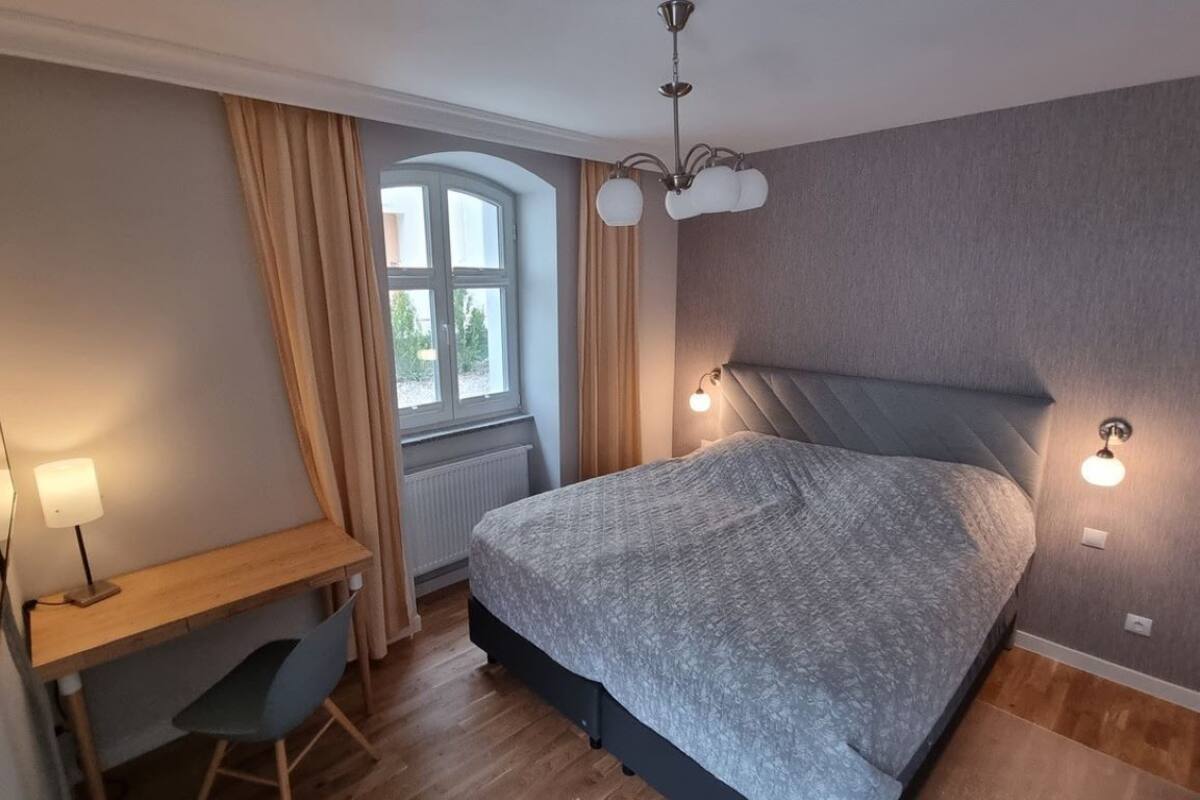 A bedroom with a bed, a desk, and a window.