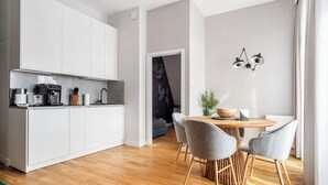 Eine moderne Küche mit weißen Schränken, einer Kaffeemaschine und einem Essbereich mit Holztisch und grauen Stühlen.