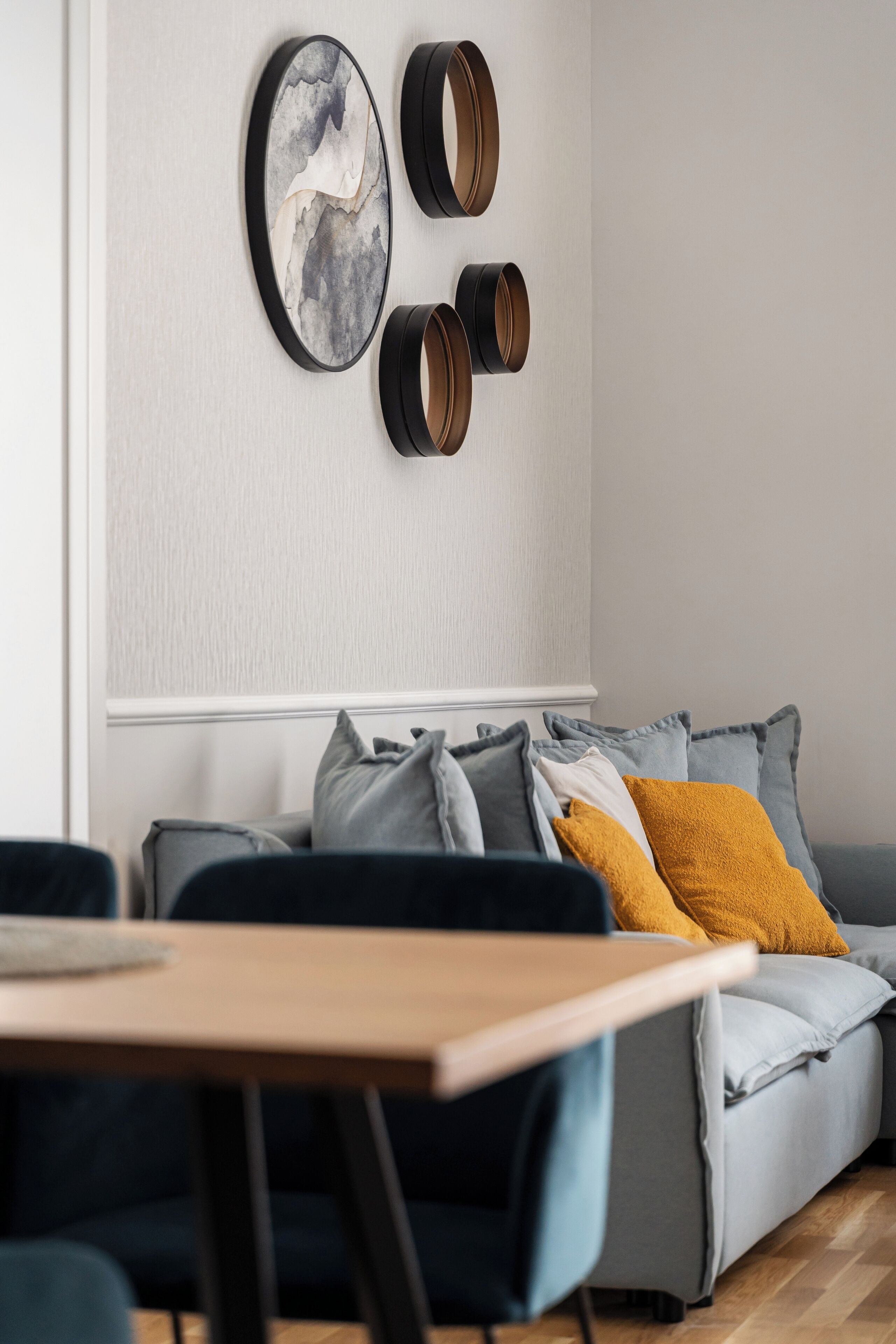 Ein modernes Wohnzimmer mit einem grauen Sofa, einem Holztisch und einem an der Wand befestigten abstrakten Kunstwerk.