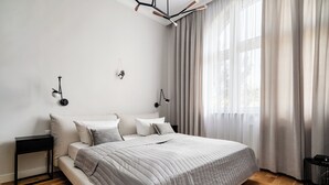 Ein modernes Schlafzimmer mit einem großen Bett, einem Nachttisch, einer Wandlampe und einem Fenster mit Vorhängen.