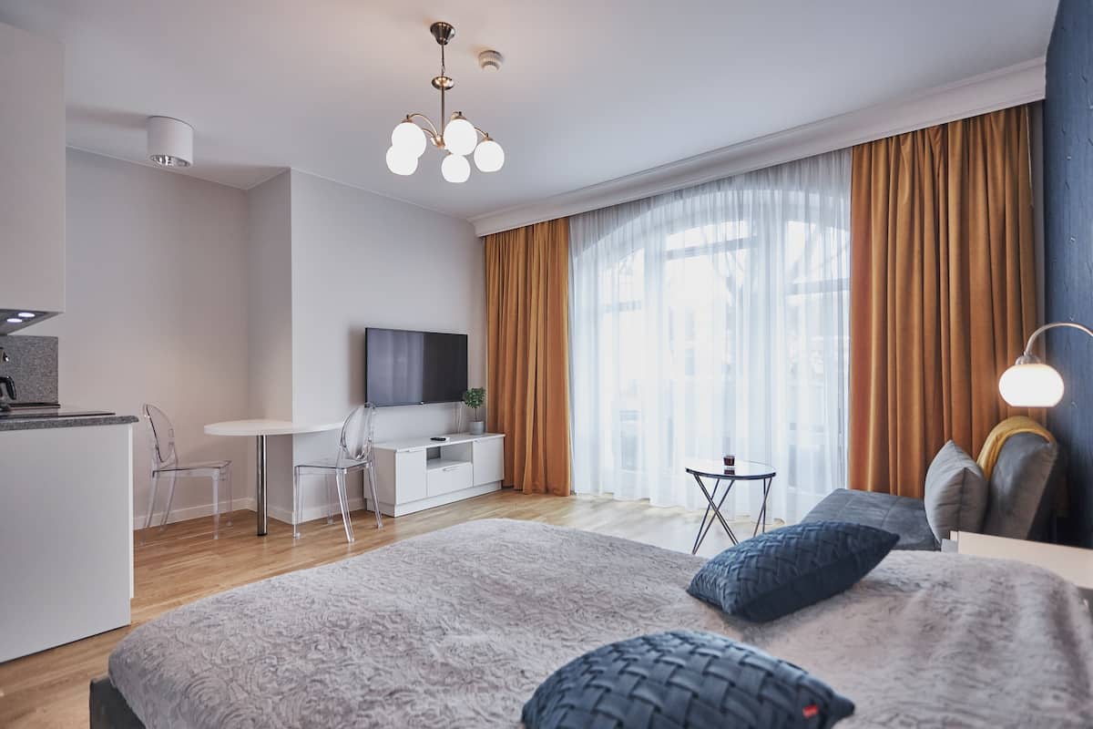 A modern hotel room with a large bed, a desk, a TV, and a dining area.