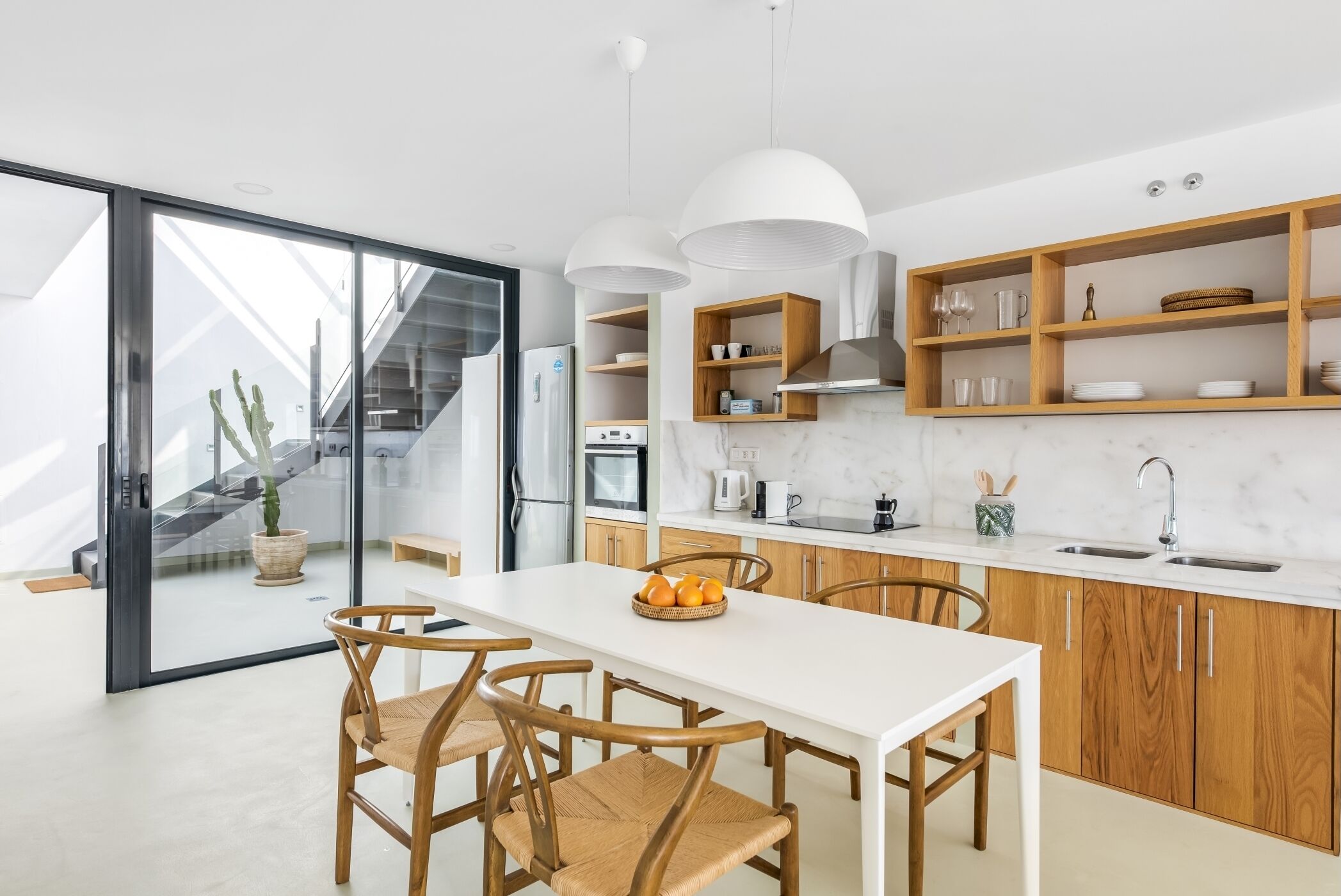 Una cocina moderna con encimera blanca, armarios de madera y una zona de comedor con mesa blanca y sillas de madera.