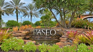 Un jardin avec un étang, des palmiers et un panneau indiquant « PASEO ».