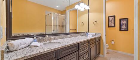A bathroom with a large mirror, dark wooden cabinets, a marble countertop, and a toilet.