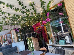 A restaurant with a sign reading 'OISE RISTORANTE,' outdoor seating with tables and chairs, and decorative plants and flowers.