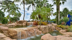 Un jardin tropical avec une cascade, des palmiers et une piscine.