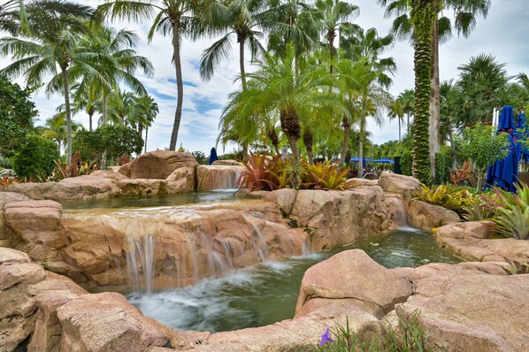 Un jardín tropical con una cascada, palmeras y una piscina.