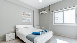 Ein modernes Schlafzimmer mit Bett, Nachttisch, Wandairconditioner und Fenster.