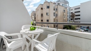 Ein Balkon mit weißen Plastikstühlen und einem Tisch, mit Blick auf einen Parkplatz und Gebäude.