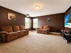 A living room with a brown sofa, a recliner, a flat-screen TV, and a wall-mounted projector.