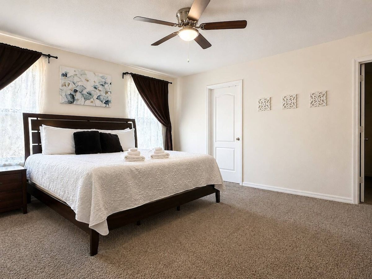 Quarto com cama, ventilador de teto, porta e janela com cortinas.