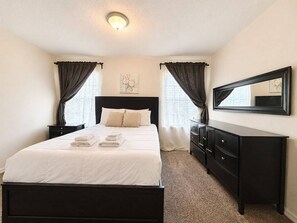 A bedroom with a bed, a dresser, a mirror, and curtains.