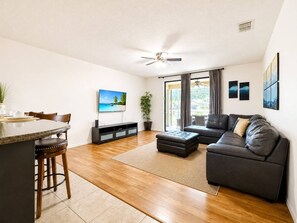 A modern living room with a dark leather sofa, a wooden dining table, and a ceiling fan.