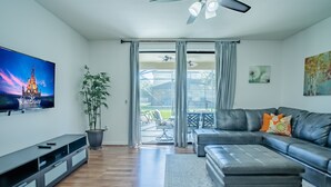 A modern living room with a flat-screen TV, a leather sofa, a potted plant, and a sliding glass door leading to an outdoor patio.