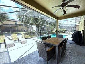 Eine Außenpatio mit Tisch und Stühlen, einem Pool und einem überdachten Bereich mit Deckenventilator.