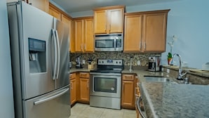 A kitchen with stainless steel appliances, wooden cabinets, a granite countertop, and a tiled backsplash.