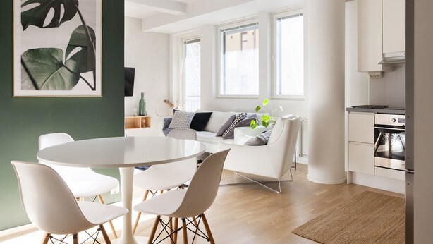 A modern kitchen with white cabinets, a built-in oven, and a dining area with a round table and white chairs. - Stylish Bright 42m2 Studio with Balcony (Helsinki)