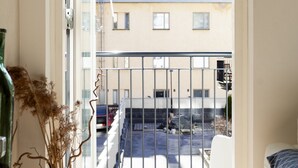 A room with a view of a courtyard, a bed, a small table, and a vase with dried plants. - Stylish Bright 42m2 Studio with Balcony (Helsinki)