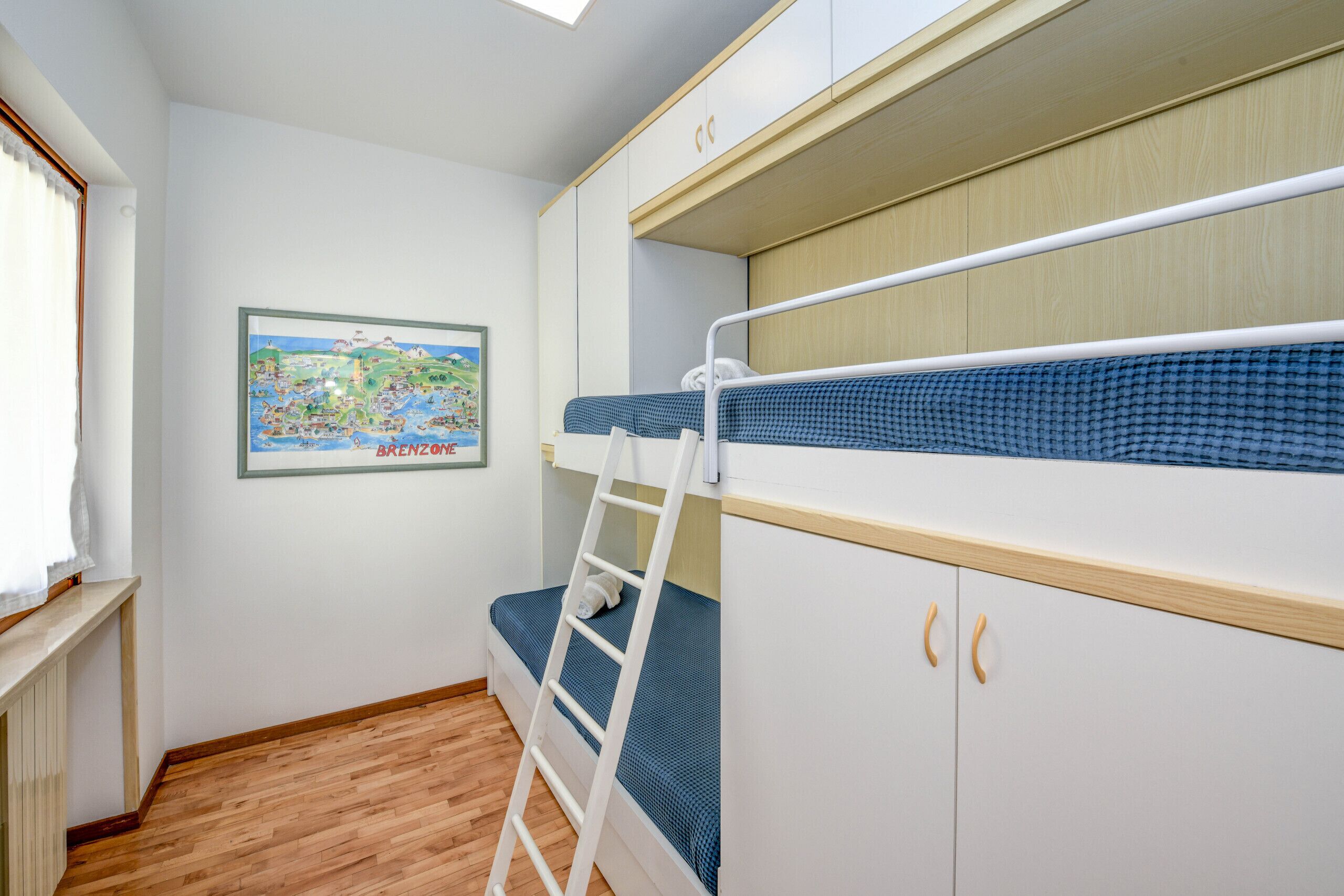 Habitación con literas, suelo de madera, una escalera y un mapa en la pared.