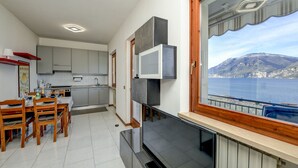 A modern kitchen with grey cabinets, a dining table set with chairs, and a large window overlooking a body of water and mountains.