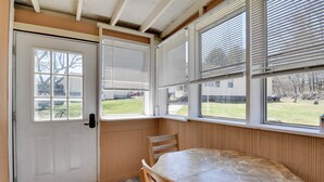 A room with a white door, a window with blinds, a wooden table, and a chair. - Shared Fire Pit & Kayaks: Catskills Lake Retreat! (Ellenville)